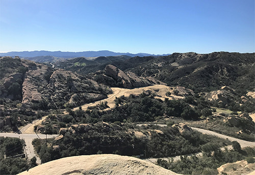 This photo shows an aerial view of the Delta Test Area, vacant of buildings or structures, with only rocks formations, trees, and dirt roads remaining.