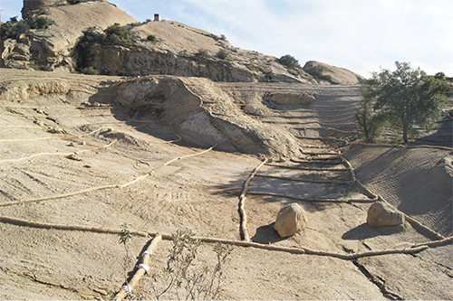 This photo shows a graded area covered with dirt, with rock formations and trees in the background.