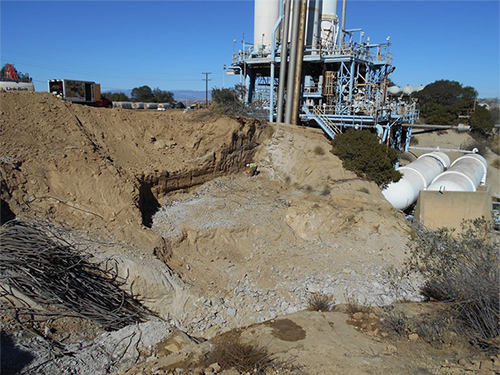 In this photo the large retaining wall has been completely removed. Small chunks of concrete remain on the ground as well as rebar, which sits in a pile off to the side. The main Bravo Test Stand is shown in the background.